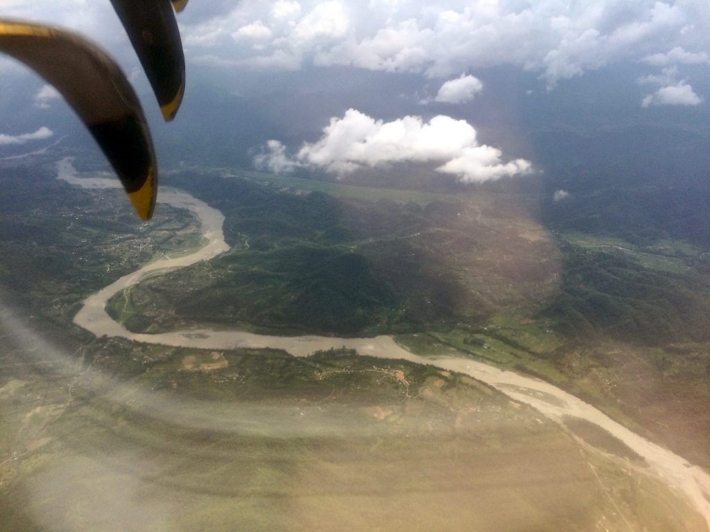 View looking out of the airplane window looking down to a winding silty river crossing Nepal countryside | Sustainable travel article on travel emissions and carbon offset