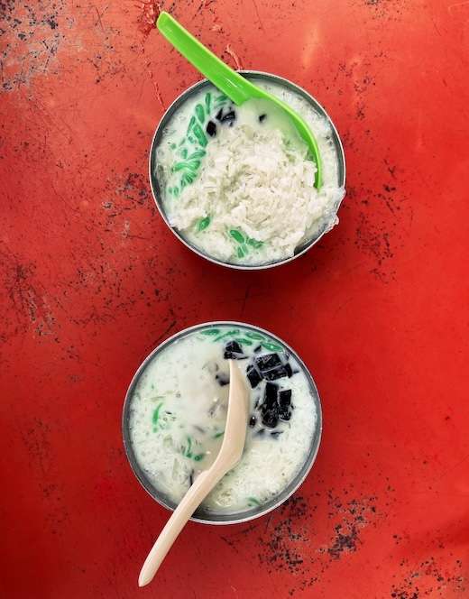 Two bowls of cendol on a red table.