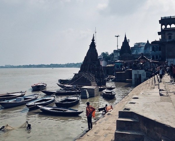 The cremation platforms and sunken Shiva temple in the distance from Manikarnika Ghat, Varanasi, India | solo travel to Benaras | Header image for travel story My Varanasi Day Tour with a Shiva Devotee - The Burning Ghat on travel blog Teja on the Horizon