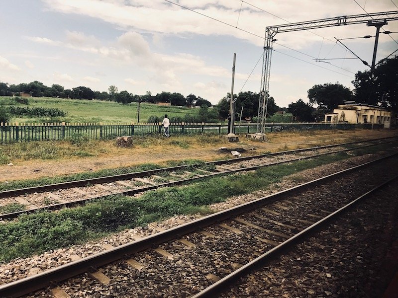 View of Indian railway train tracks against countryside from inside a train cabin | Travel sustainably by taking the train