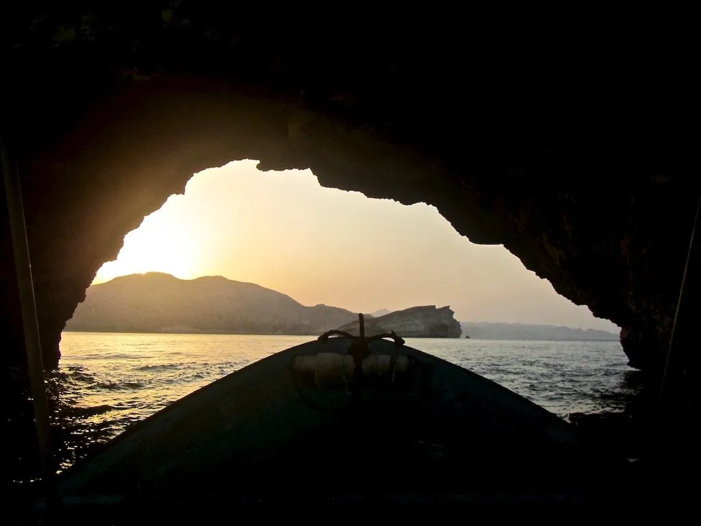 Travel story "An Omani Girl Unveils Stereotypes of Omani Life and History" on Teja on the Horizon | Boat exiting a sea cave arch towards sunset