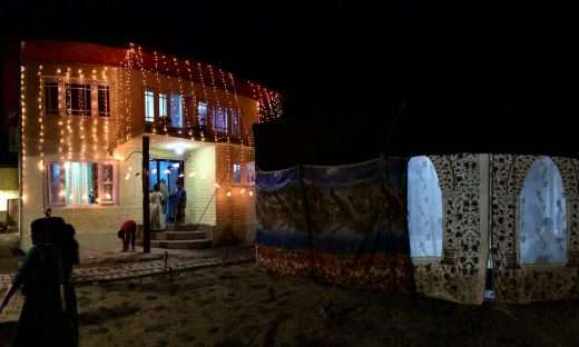 Village compound in Srinagar decked out for a wedding. The house is hung with warm orange fairy lights, and a traditional eating tent featuring Kashmir's hamdan embroidery is set up nearby.