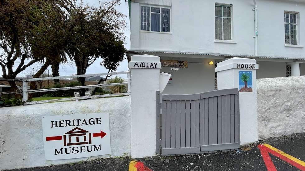 Closed entry gate to Amlay House in Simon's Town. A signage marking 'Heritage Museum' is fixed on the whitewashed stone fence on the left of the gate with an arrow pointing to it.