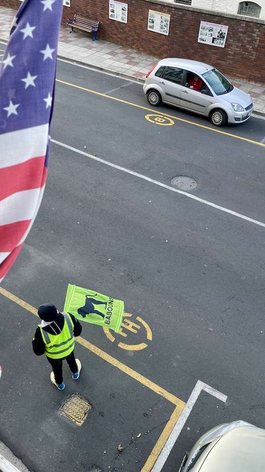 View from the Central Hotel Guest House balcony looking down at a crossing guard. The guard is wearing a high visibility vest and a similar coloured flag with a silhouette of a baboon and the word 'baboon'.