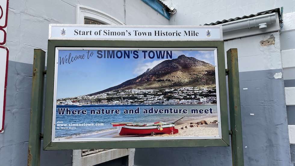Signage outside the railway station welcoming visitors to Simon's Town with the tagline 'Where nature and adventure meet', and marking the start of Simon's Town Historic Mile.