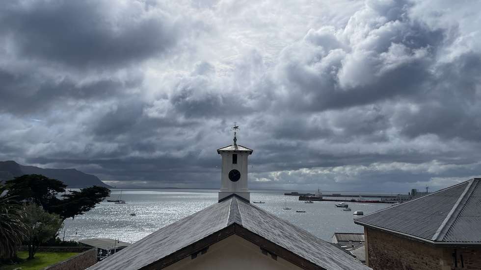 View across the rooftop of the South African Naval Museum from St Georges Street. A weather vane rises at the far end of the roof peak. Simon's Bay lies beyond.